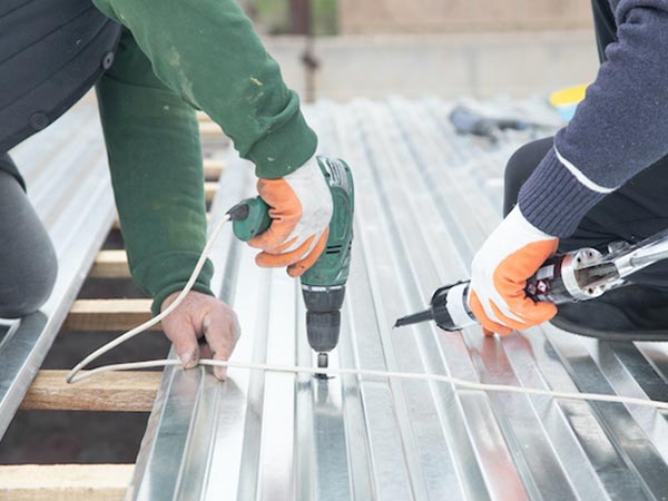 Metal-Roof-Leak-Repair-Canton-GA-Georgia-1 | Rise Residential Roofing Two workers with gloves drill and fasten metal roof panels on a corrugated roof.