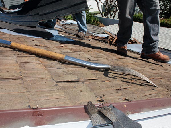 Roof-Leak-Repair-Cartersville-GA-Georgia-2 | Rise Residential Roofing Two workers on a sloped roof remove shingles; a crowbar-like tool and a long-handled chisel lie on the surface nearby.