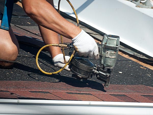 Roof-Repairs-Cartersville-GA-Georgia-2 | Rise Residential Roofing Worker in white gloves using a pneumatic roofing nailer on brown shingles on a sloped roof.